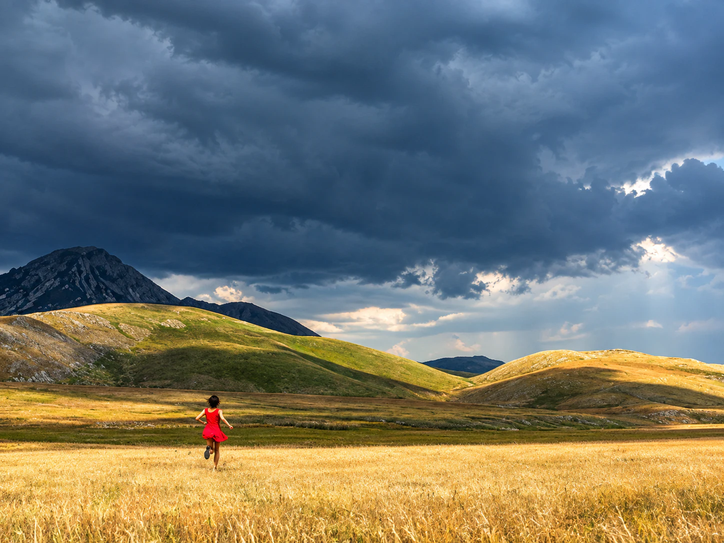 Figura in rosso che corre in un paesaggio montano sotto un cielo temporalesco